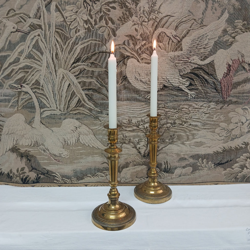 Two lit candles in French antique brass candlesticks tapestry backdrop at French Originals NZ